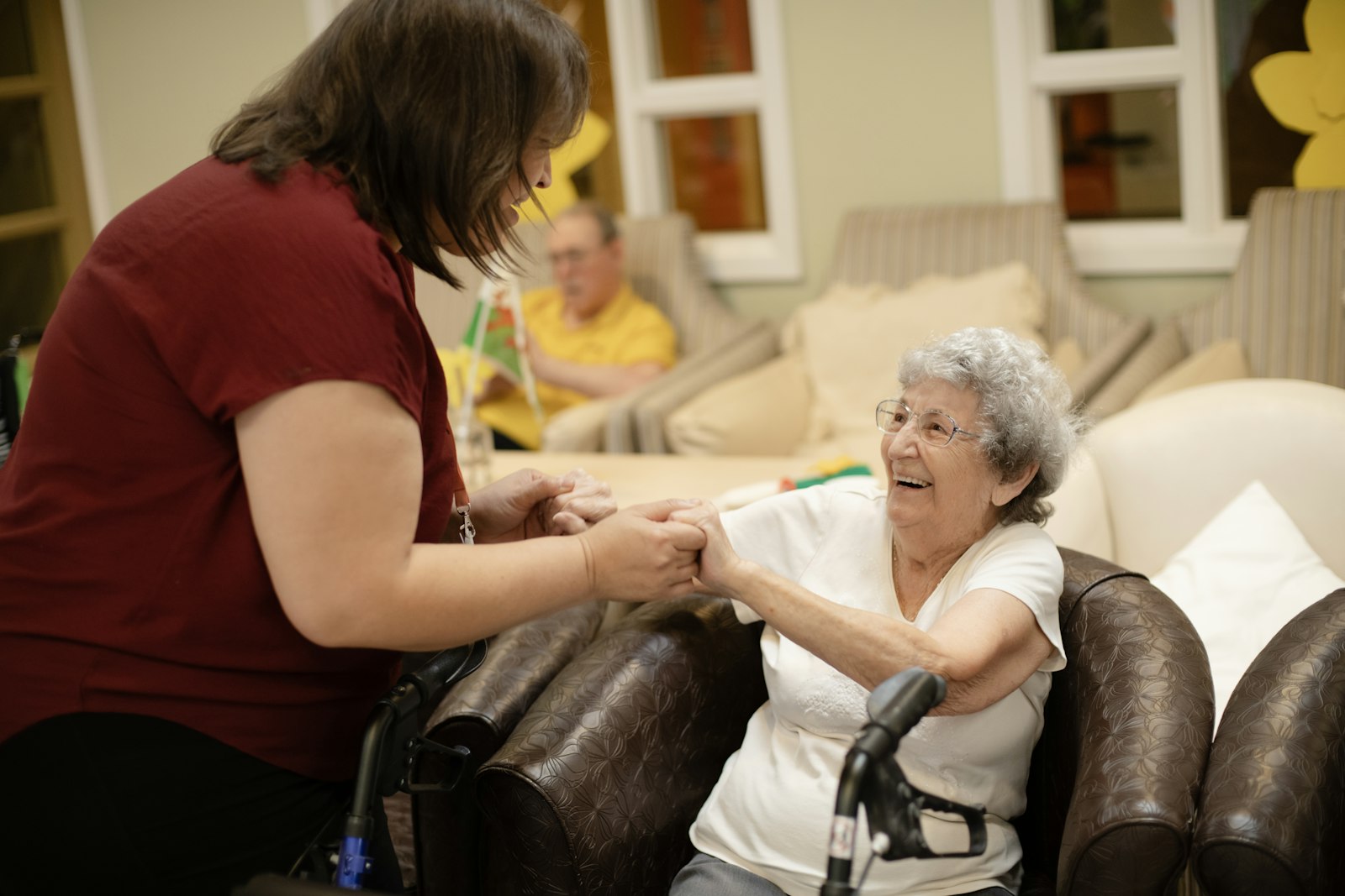 A care worker holding hands with a smiling resident in a care home lounge