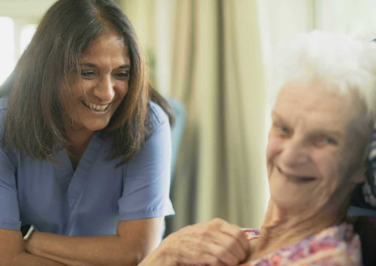 A smiling care worker sharing a laugh with an older woman